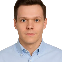 Młody mężczyzna o krótkich brązowych włosach i niebieskich oczach ma na sobie jasnoniebieską koszulę z kołnierzykiem, patrzy prosto w kamerę z neutralnym wyrazem twarzy, a jego zdjęcie znajduje się na białym tle, idealnym na zdjęcie profilowe w serwisie WordPress.