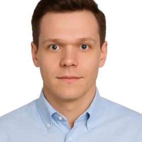 Młody mężczyzna o krótkich brązowych włosach i niebieskich oczach ma na sobie jasnoniebieską koszulę z kołnierzykiem, patrzy prosto w kamerę z neutralnym wyrazem twarzy, a jego zdjęcie znajduje się na białym tle, idealnym na zdjęcie profilowe w serwisie WordPress.